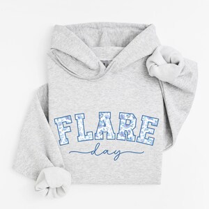 May include: Gray hooded sweatshirt with a blue and white floral print graphic that says "FLARE day" in a collegiate style font.