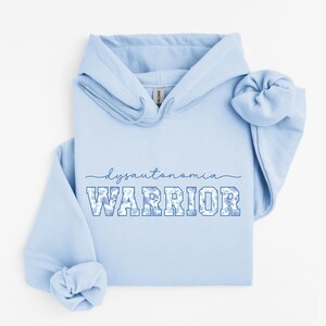 May include: Light blue hoodie with the text "dysautonomia warrior" in blue letters with a floral pattern. The hoodie has a drawstring hood and a kangaroo pocket.