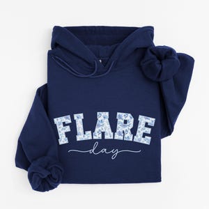 May include: A navy blue hoodie with a white floral print that says "FLARE day" on the front.
