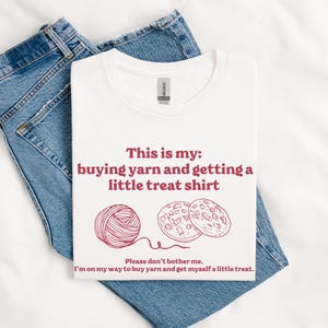 May include: White t-shirt with red text that says "This is my: buying yarn and getting a little treat shirt". There is a drawing of a ball of yarn and two cookies.