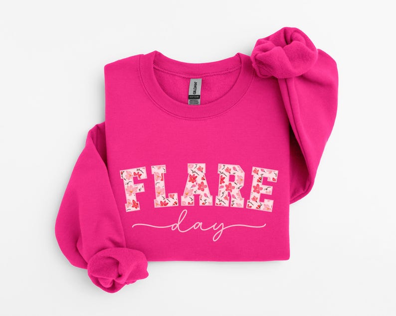 May include: A pink sweatshirt with the text "FLARE day" in white letters with a floral pattern. The letters are in a bold, blocky font.