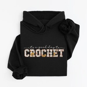 Puede incluir: Sudadera con capucha negra con el texto "it's a good day to CROCHET" en letras blancas y de estampado floral.