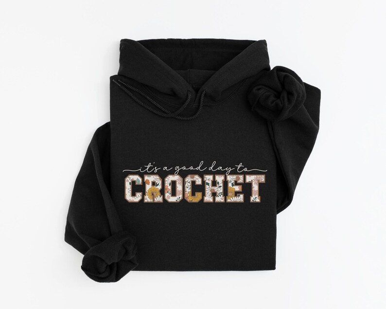 Puede incluir: Sudadera con capucha negra con el texto "it's a good day to CROCHET" en letras blancas y de estampado floral.