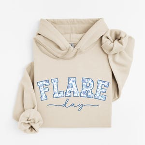 May include: A beige hoodie with a blue and white floral print design that says "FLARE day" on the front.