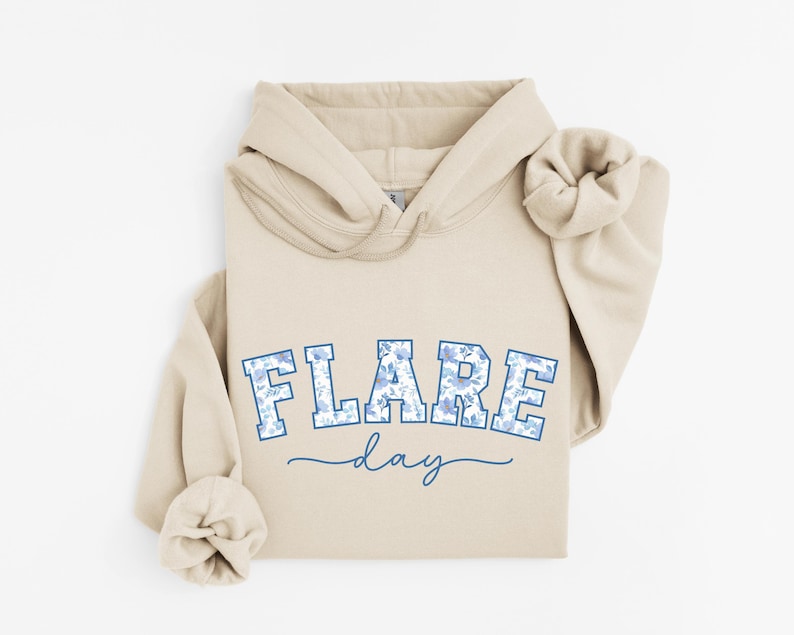 May include: A beige hoodie with a blue and white floral print design that says "FLARE day" on the front.