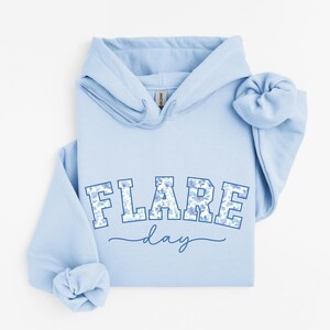 May include: Light blue hoodie with a floral print design that says "FLARE day" in a blue and white collegiate font.