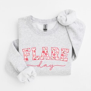 May include: A gray sweatshirt with the text "FLARE day" printed in pink with a floral pattern. The text is in a bold, blocky font.