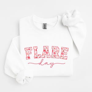 May include: White sweatshirt with a pink floral print that says "FLARE day" in a pink outline.