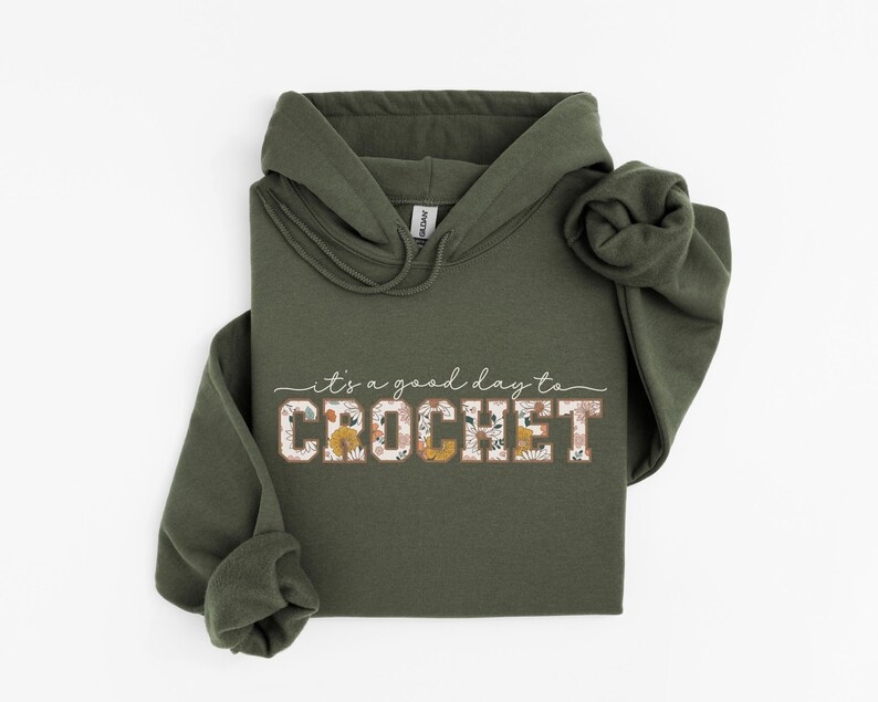 Puede incluir: Una sudadera con capucha verde con el texto "it's a good day to CROCHET" en blanco con detalles florales.
