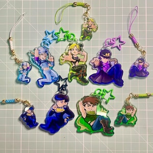 Puede incluir: Una colección de diez dijes de acrílico con varios personajes de estilo anime en poses dinámicas. Los dijes incluyen cierres en forma de estrella y cordones trenzados de colores en tonos verde, azul, morado y blanco sobre una cuadrícula.