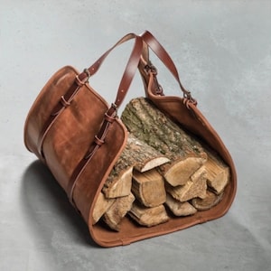 May include: A brown leather firewood carrier with two handles and a large opening for carrying logs. The carrier is filled with stacked firewood.