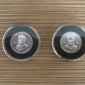 May include: Two silver coins in clear plastic cases. The coins feature portraits of Benjamin Harrison, the 23rd President of the United States, and Theodore Roosevelt, the 26th President of the United States. The coins are inscribed with the years of their presidencies.