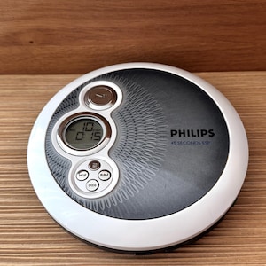 May include: A silver and black Philips portable CD player with a digital display showing "10 0:15". The device has a white border and the text "45 SECONDS ESP". Buttons include play/pause, skip, and DDB.