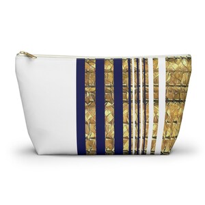 May include: White zippered pouch with a navy blue and gold striped design. The stripes are made of a textured fabric.