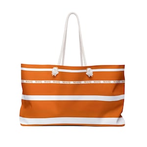 May include: Large orange and white striped tote bag with white rope handles. The bag features the word "MAHJ" printed repeatedly in a horizontal band across the center. The bag is designed for carrying items and has a simple, clean aesthetic.