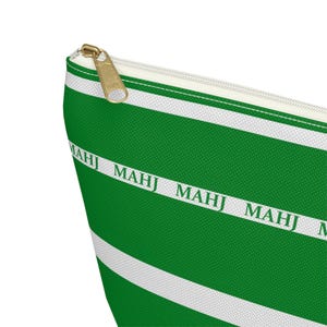 May include: Green and white striped cosmetic bag with a gold zipper. The bag features the word "MAHJ" printed in white along the green stripes. The bag is made of a textured fabric.