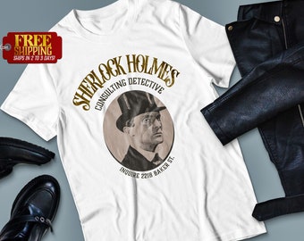 May include: White t-shirt with a gold graphic of Sherlock Holmes, a consulting detective. The graphic includes a portrait of Sherlock Holmes wearing a hat and a quote: "Inquire 221B Baker St."