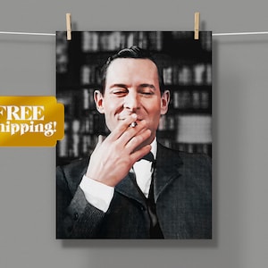 Puede incluir: Un retrato en blanco y negro de un hombre con traje, sonriendo y sosteniendo un cigarrillo en la mano. Está de pie frente a una estantería.