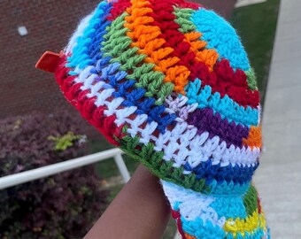 May include: A colorful crocheted hat with a rainbow pattern. The hat has a brim and a strap.