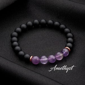 May include: A black beaded bracelet with amethyst stones and rose gold accents. The bracelet has the word "Amethyst" written below it.