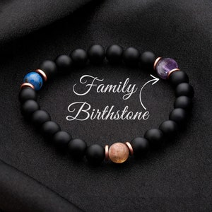 May include: Black beaded bracelet with a variety of birthstones, including amethyst, lapis lazuli, and sunstone. The bracelet is labeled "Family Birthstone".