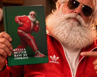 May include: A green hardback book titled STELLA, BETTER HAVE MY COOKIES featuring a graphic of a person in a red tracksuit. The book is held by a person with a white beard wearing a red tracksuit, white socks with logos, and red trainers.