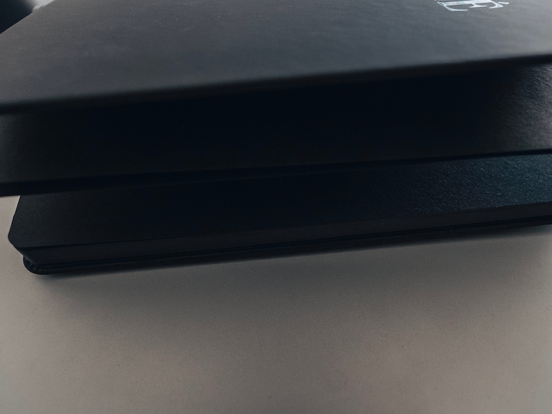 May include: Three black notebooks stacked on top of each other. The top notebook has a white letter "H" embossed on the cover.