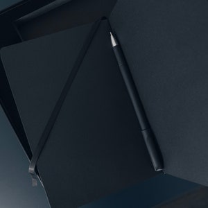 May include: A black notebook with a black pen inside, both are in a black box.