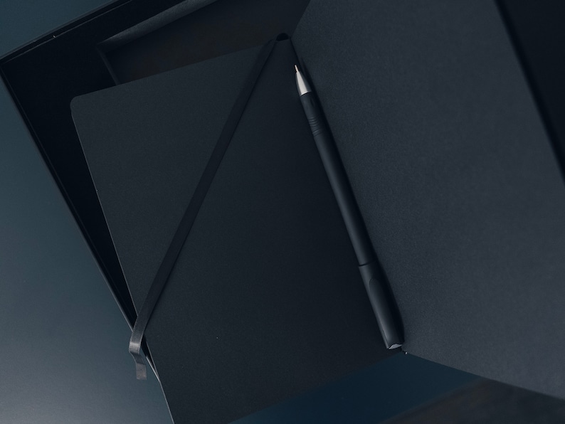 May include: A black notebook with a black pen inside, both are in a black box.