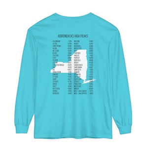 May include: A turquoise long-sleeve t-shirt with a white outline of the state of New York. The text "ADIRONDACKS HIGH PEAKS" is at the top of the shirt. The names of the high peaks in the Adirondack Mountains are listed next to their elevations in feet.