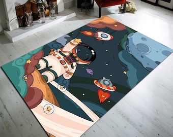 Puede incluir: Una alfombra colorida con un astronauta flotando en el espacio. La alfombra presenta un esquema de colores azul, verde y naranja con estrellas, planetas y una nave espacial.