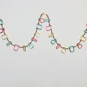 May include: A festive garland with red, green, and gold metallic ornaments shaped like beakers and flasks. The garland is strung with small red beads.