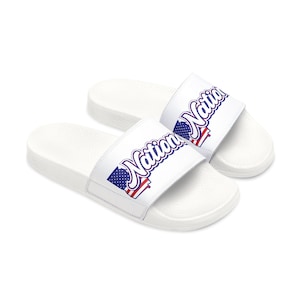 Puede incluir: Sandalias deslizantes blancas con la palabra "Nation" en escritura azul y un diseño de bandera americana roja, blanca y azul. Las sandalias son de material liso, adecuadas para uso casual.