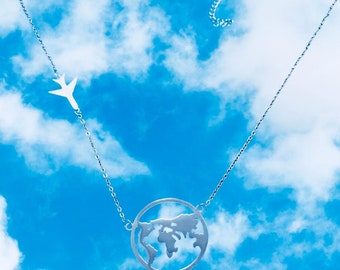 May include: A silver necklace with a world map pendant and a small airplane charm hanging from a silver chain against a blue sky with white clouds.