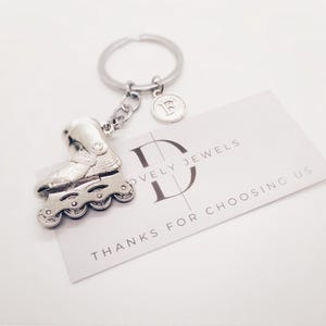 Op de afbeelding: Zilveren rolstoelschlüsselhanger met een zilveren bedel met de tekst "D" en "Lovely Jewels" op een witte kaart met de tekst "Bedankt voor het kiezen voor ons".