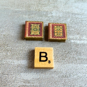 May include: Two miniature books with ornate red and gold covers, and a wooden tile with the letter "B" and the number "3" printed on it. The books have detailed floral designs.