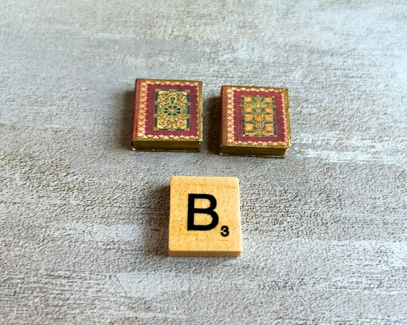 May include: Two miniature books with ornate red and gold covers, and a wooden tile with the letter "B" and the number "3" printed on it. The books have detailed floral designs.