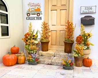 May include: A miniature dollhouse porch scene featuring a light wood door, a mailbox, and a sign reading 7206 Peach Street. The display includes several potted floral arrangements in autumn colors, small orange pumpkins, and a wall graphic reading Autumn Collection.