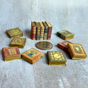 May include: A collection of miniature books in various colors and designs. Some books are stacked, while others are scattered around a coin. The books have gold-colored edges and decorative covers with floral and geometric patterns.
