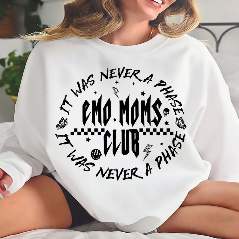 Puede incluir: Sudadera blanca con un gr&aacute;fico negro que dice "It was never a phase Emo Moms Club It was never a phase". El gr&aacute;fico est&aacute; rodeado de estrellas, rayos y mariposas.