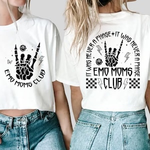 Puede incluir: Dos camisetas blancas con un dise&ntilde;o gr&aacute;fico negro de una mano de esqueleto haciendo un signo de rock and roll. El texto en las camisetas dice "Emo Moms Club" y "It was never a phase - It was never a phase - Emo Moms Club".