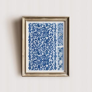 May include: Framed artwork featuring a blue and white floral pattern. The print has a detailed design with swirling leaves and flowers. The frame is gold-colored, adding a touch of elegance to the artwork. The artwork is displayed on a white wall.