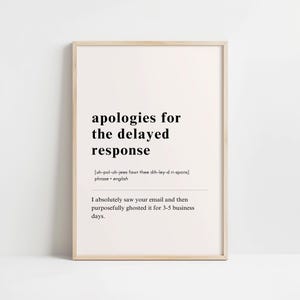 May include: A framed print with the text "apologies for the delayed response." The text includes a phonetic pronunciation and a humorous statement about ignoring emails for 3-5 business days. The frame is a light wood color.