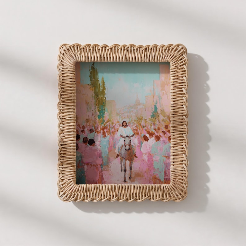 May include: A framed print depicting a religious scene with a figure on a donkey, surrounded by a crowd. The artwork features pastel colors and is set within a woven, rectangular frame. The frame is made of a light brown material.