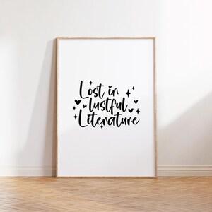 Puede incluir: Una impresi&oacute;n enmarcada con el texto "Lost in lustful literature" en escritura negra con peque&ntilde;os corazones y estrellas alrededor de las palabras. La impresi&oacute;n est&aacute; sobre un fondo blanco y est&aacute; enmarcada en un marco de madera claro.
