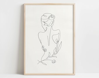 May include: A framed minimalist line art print. The artwork shows the back of a person with a bun hairstyle, arms crossed, and a flower. The black lines contrast against the off-white background, creating a simple yet elegant design.