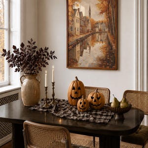 May include: A dining table setting featuring three carved jack-o'-lantern pumpkins, a black and white plaid table runner, two tall taper candles in brass holders, a large ceramic vase with dark foliage, and a bowl containing three green pears.