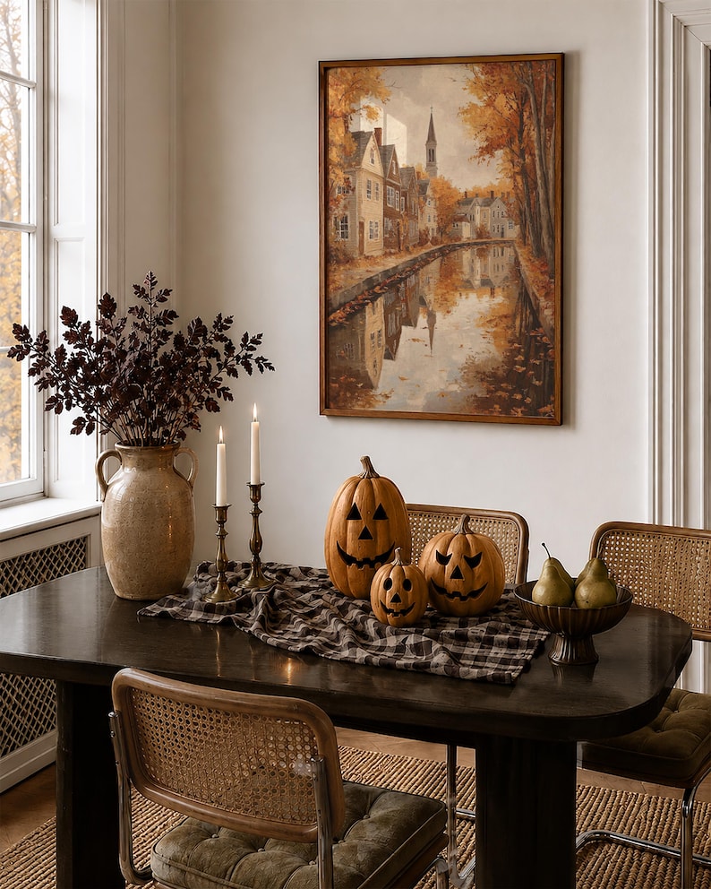May include: A dining table setting featuring three carved jack-o'-lantern pumpkins, a black and white plaid table runner, two tall taper candles in brass holders, a large ceramic vase with dark foliage, and a bowl containing three green pears.