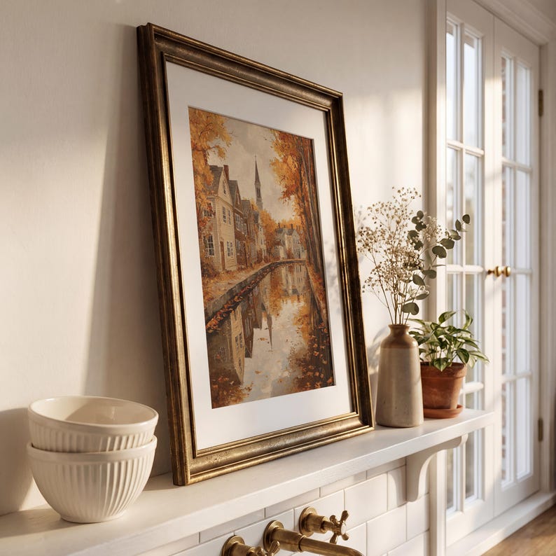 May include: A framed vertical wall art print depicting a canal scene with autumn foliage and buildings, housed in a dark metallic frame with a white mat. The artwork features warm orange and brown tones reflecting in the water surface.