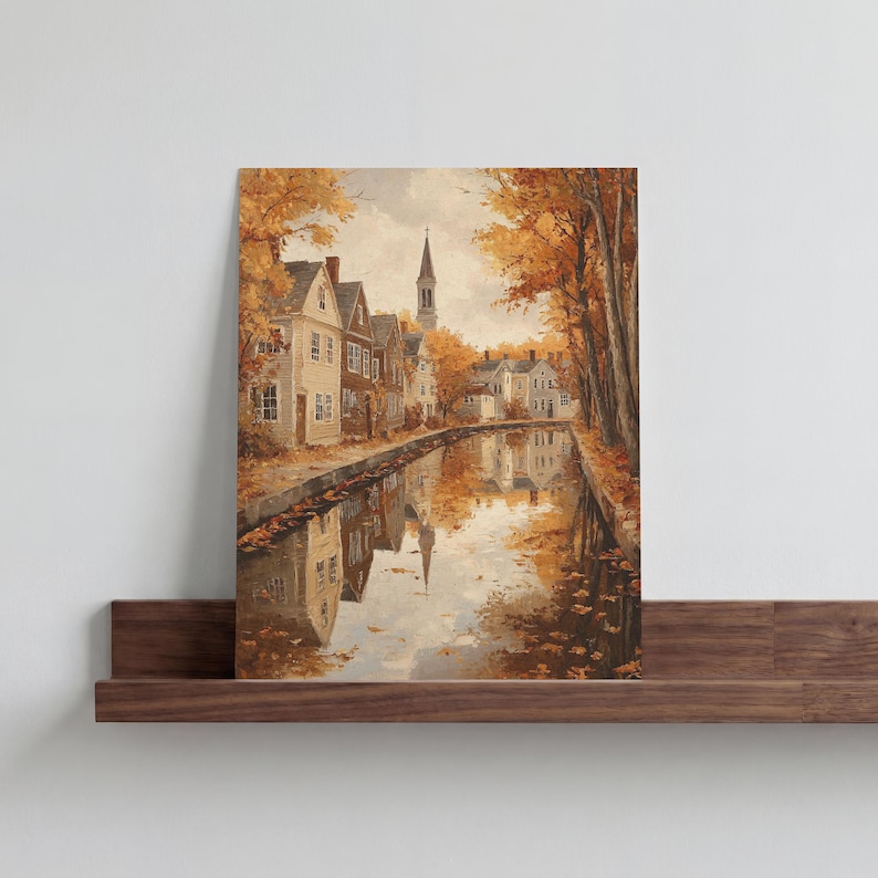May include: A rectangular wall art print depicting a canal-side town scene during autumn. The image features light-colored houses, a tall church steeple, and trees with orange and yellow foliage, all reflected in the calm water of the canal.